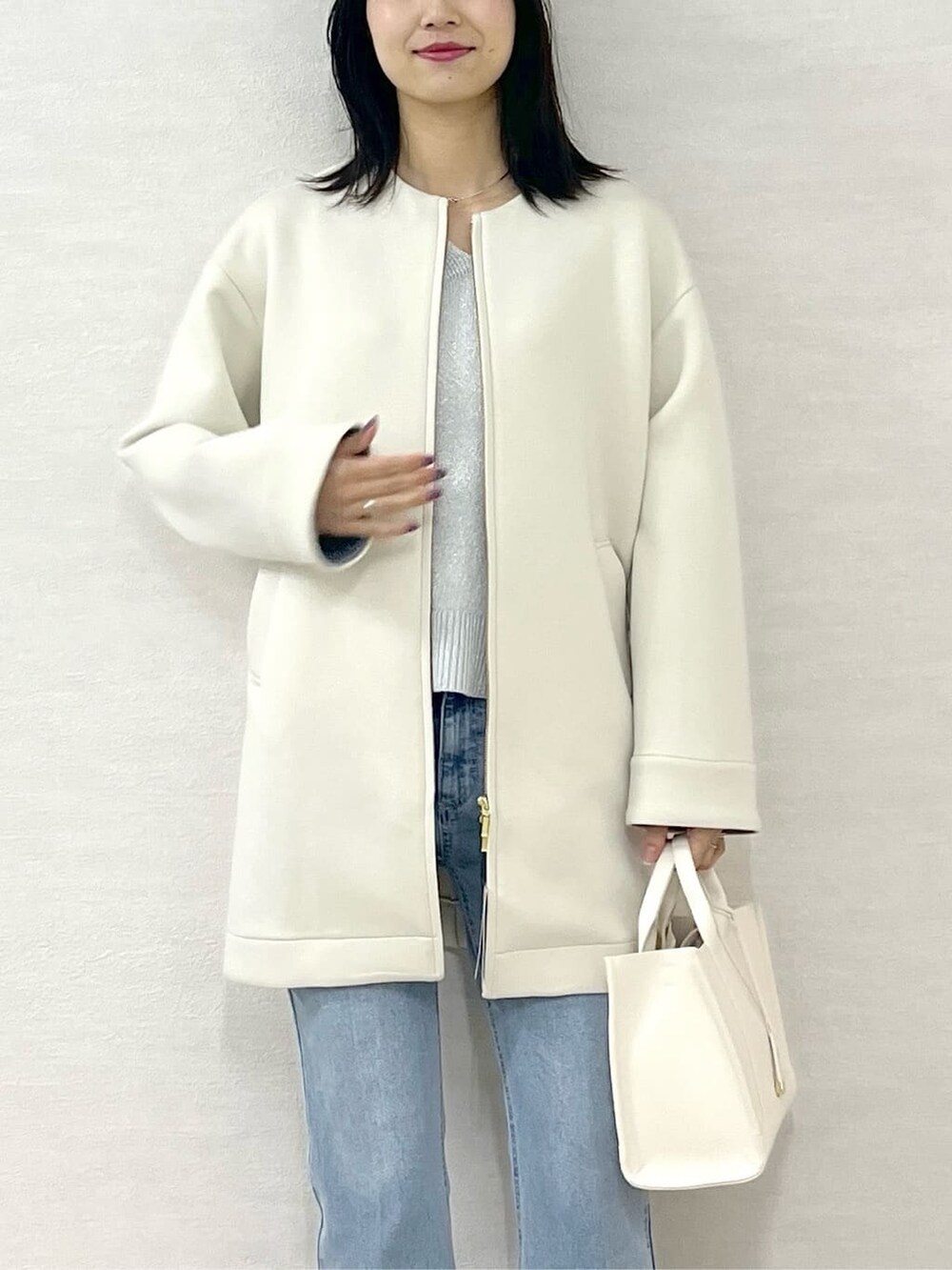 ホワイト系のノーカラーコート、シルバー系のニット/セーター、ブルー系のデニムパンツを着用したレディースの冬コーディネートの6枚目の写真