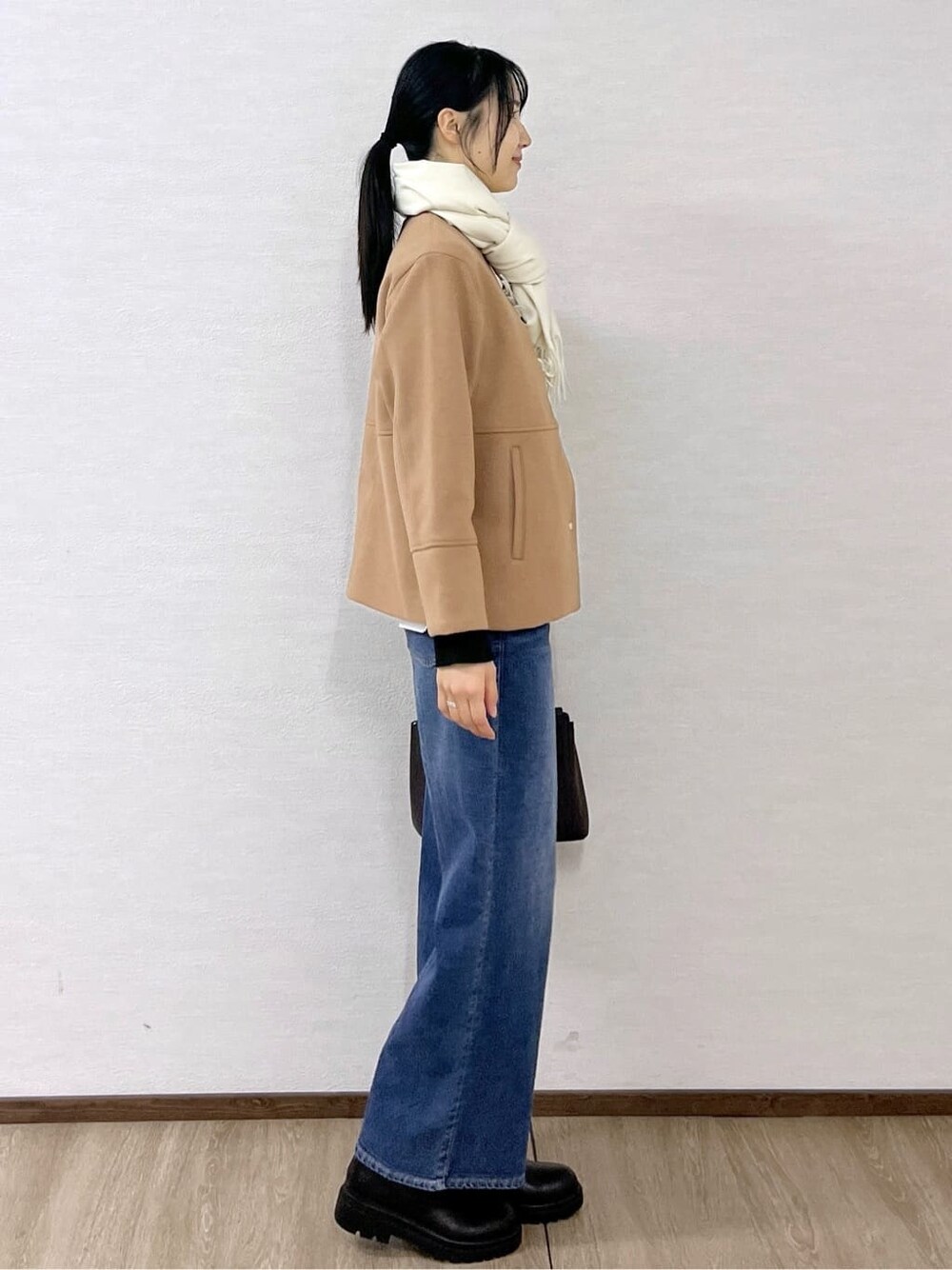 イエロー系のノーカラーコート、ブラック系のニット/セーター、ブルー系のデニムパンツを着用したレディースの秋コーディネートの5枚目の写真
