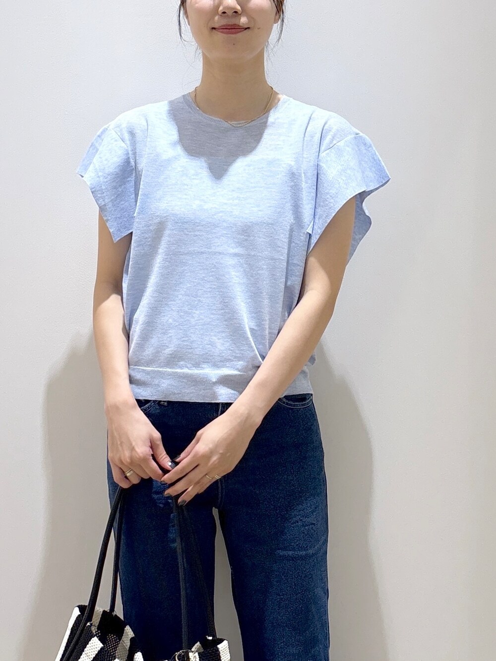 ブルー系のニット/セーター、ブルー系のデニムパンツ、ブラック系のトートバッグを着用したレディースの夏コーディネートの6枚目の写真