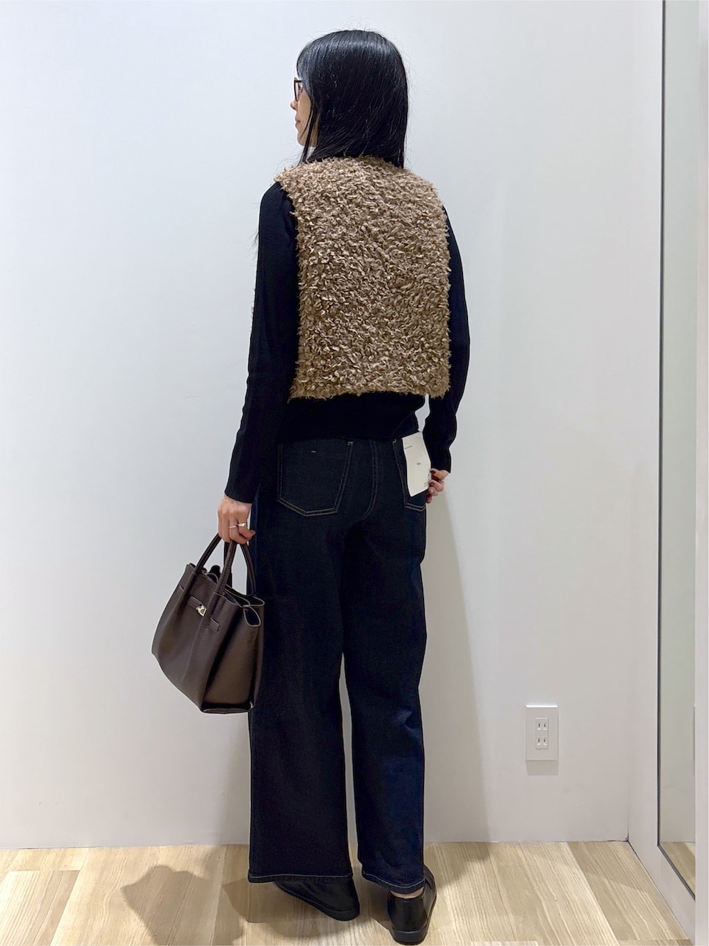 ブラウン系のベスト、ブラック系のニット/セーター、ブルー系のデニムパンツを着用したレディースの秋コーディネートの4枚目の写真