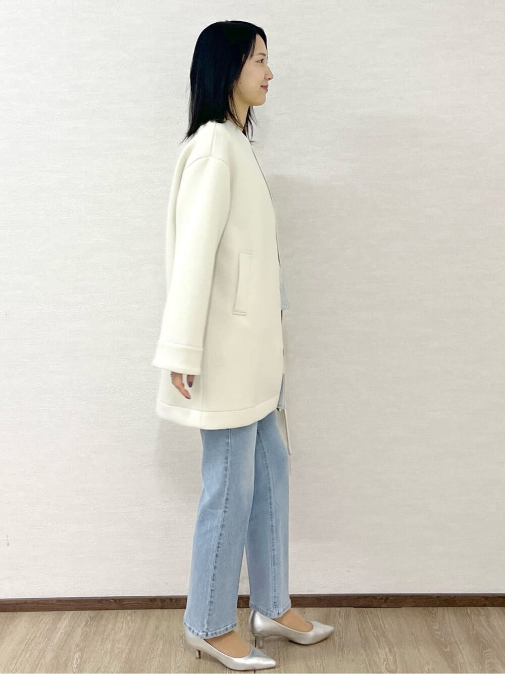 ホワイト系のノーカラーコート、シルバー系のニット/セーター、ブルー系のデニムパンツを着用したレディースの冬コーディネートの5枚目の写真