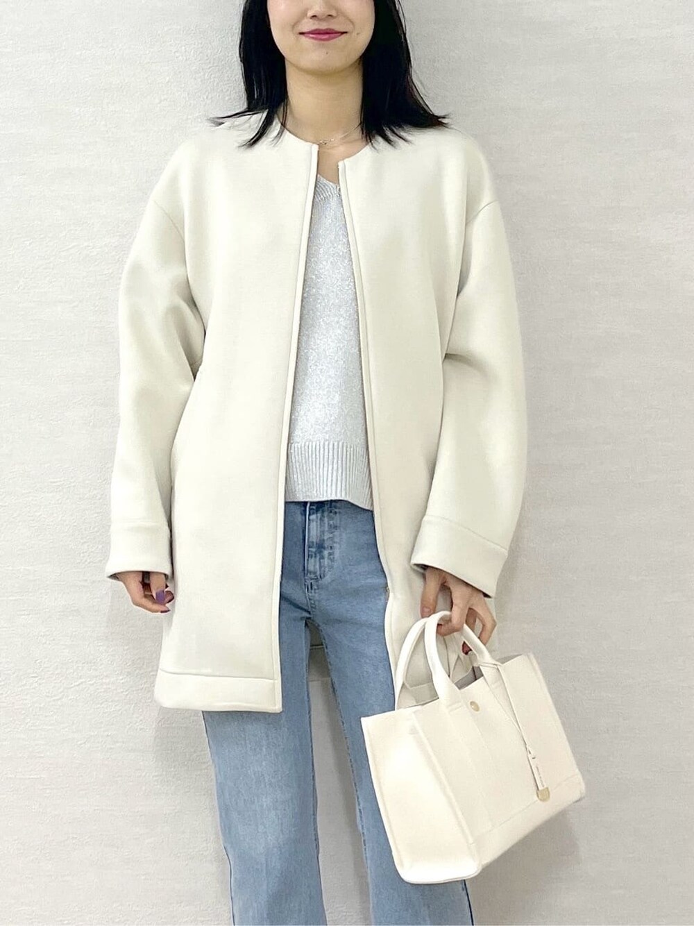 ホワイト系のノーカラーコート、シルバー系のニット/セーター、ブルー系のデニムパンツを着用したレディースの冬コーディネートの7枚目の写真