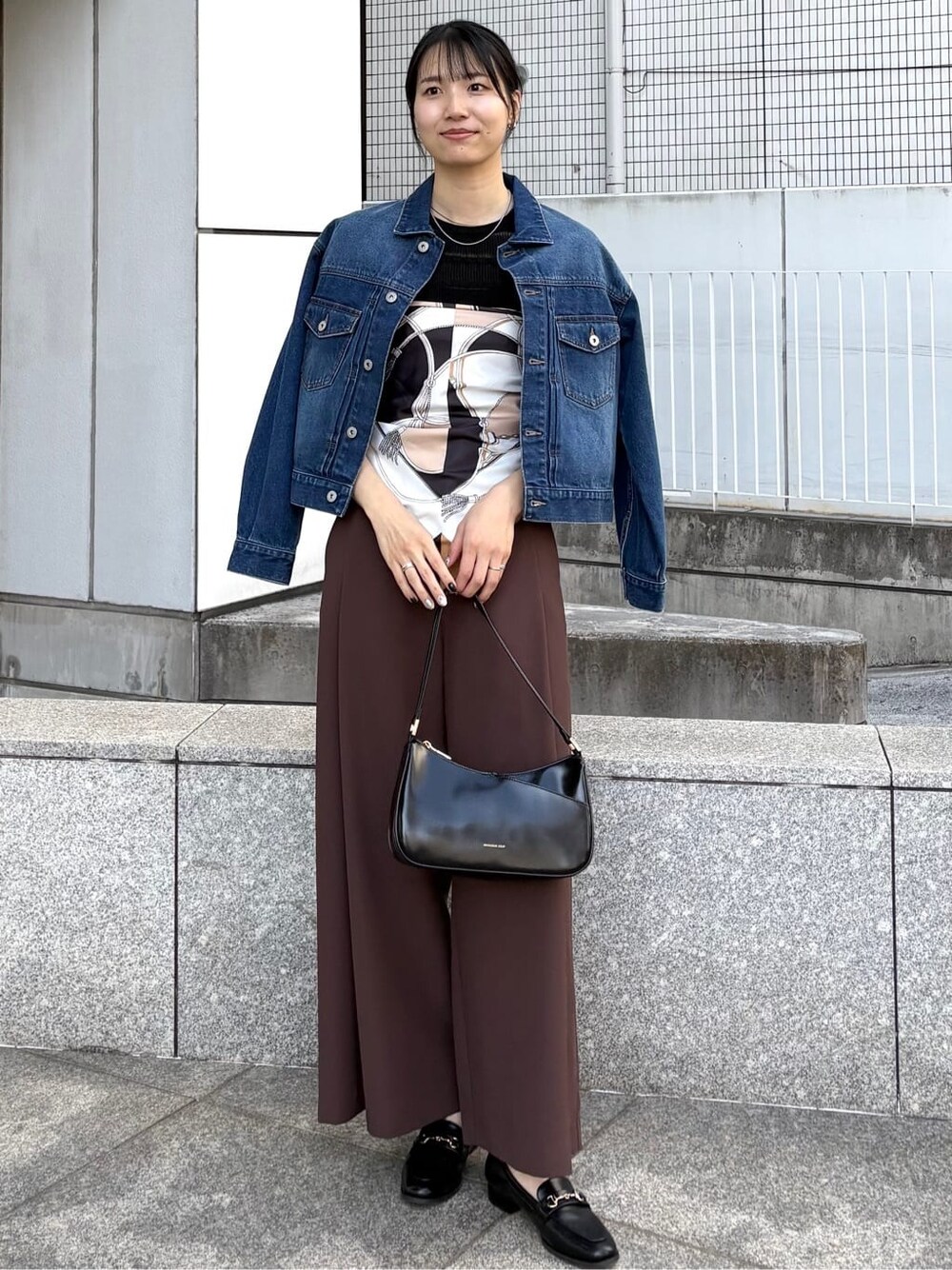 ブルー系のデニムジャケット、ブラック系のニット/セーター、ブラック系のショルダーバッグを着用したレディースの春コーディネートの3枚目の写真