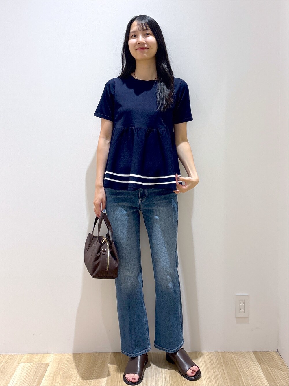 ブルー系のニット/セーター、ブルー系のデニムパンツ、ブラウン系のボストンバッグを着用したレディースの夏コーディネートの2枚目の写真
