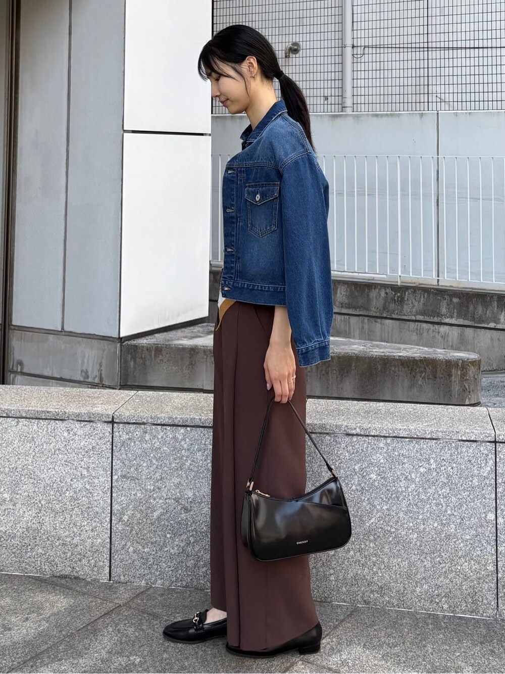 ブルー系のデニムジャケット、ブラック系のニット/セーター、ブラック系のショルダーバッグを着用したレディースの春コーディネートの4枚目の写真