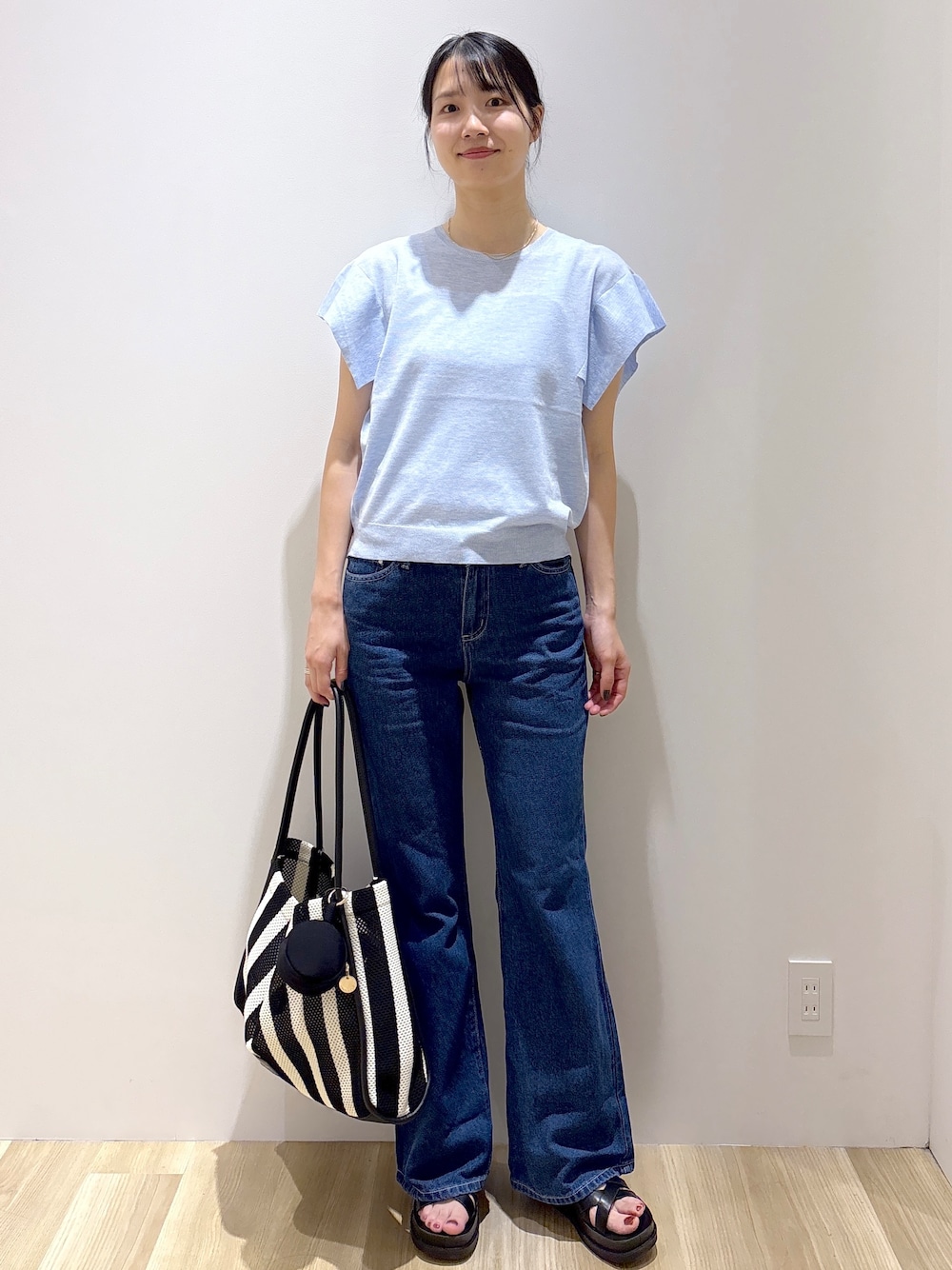 ブルー系のニット/セーター、ブルー系のデニムパンツ、ブラック系のトートバッグを着用したレディースの夏コーディネートの2枚目の写真