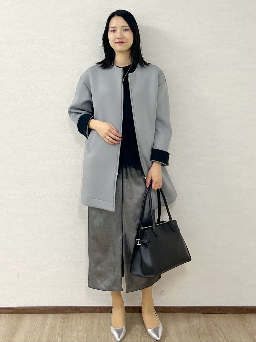 グレー系のノーカラーコート、ブラック系のTシャツ/カットソー、ブラック系のスカートを着用したレディースの冬コーディネートの3枚目の写真