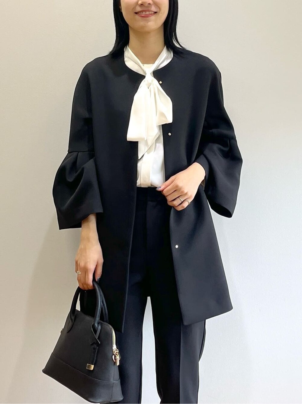 ブラック系のノーカラーコート、ホワイト系のシャツ/ブラウス、ブラック系のその他パンツを着用したレディースの秋コーディネートの7枚目の写真