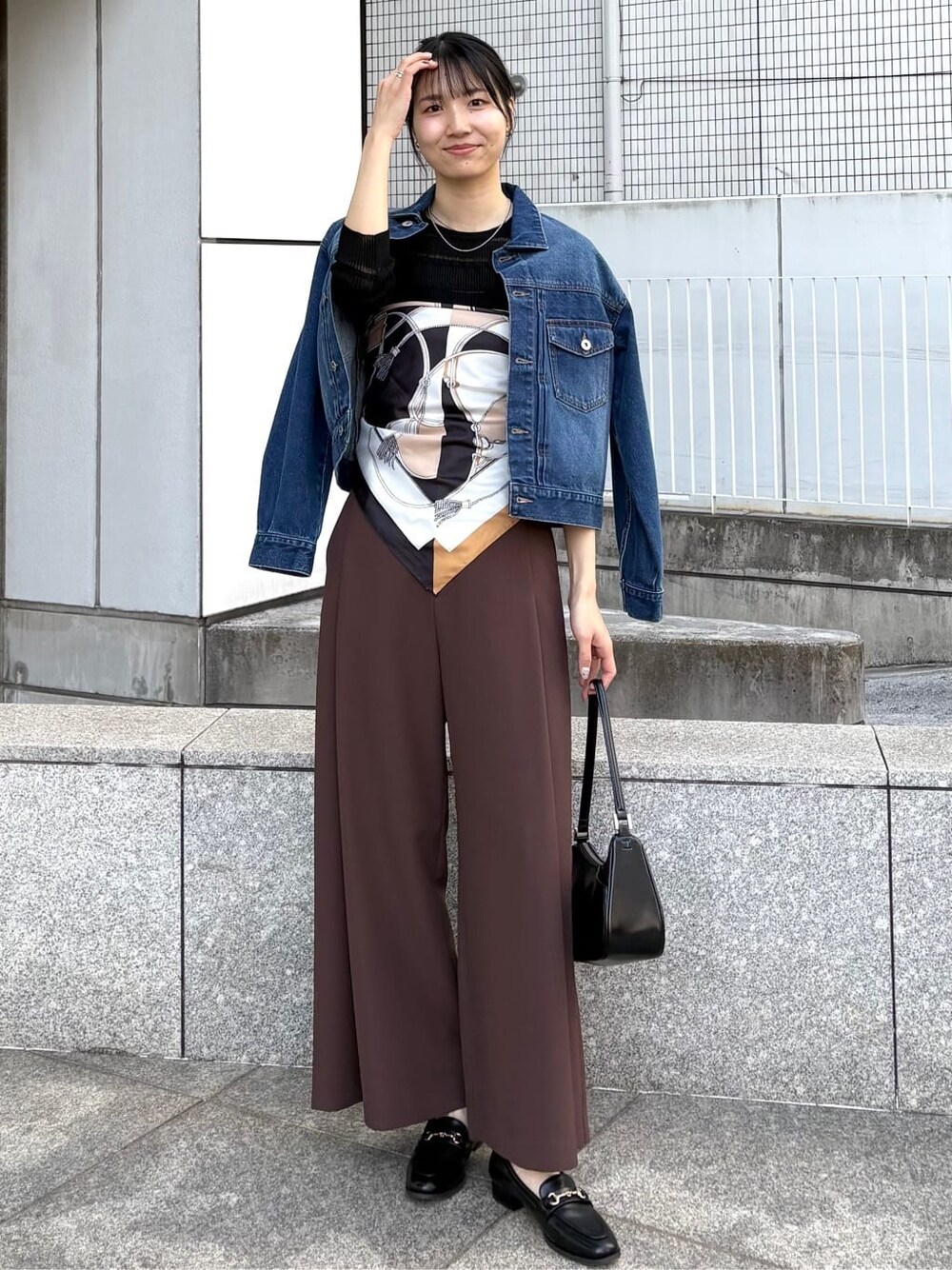 ブルー系のデニムジャケット、ブラック系のニット/セーター、ブラック系のショルダーバッグを着用したレディースの春コーディネートの2枚目の写真