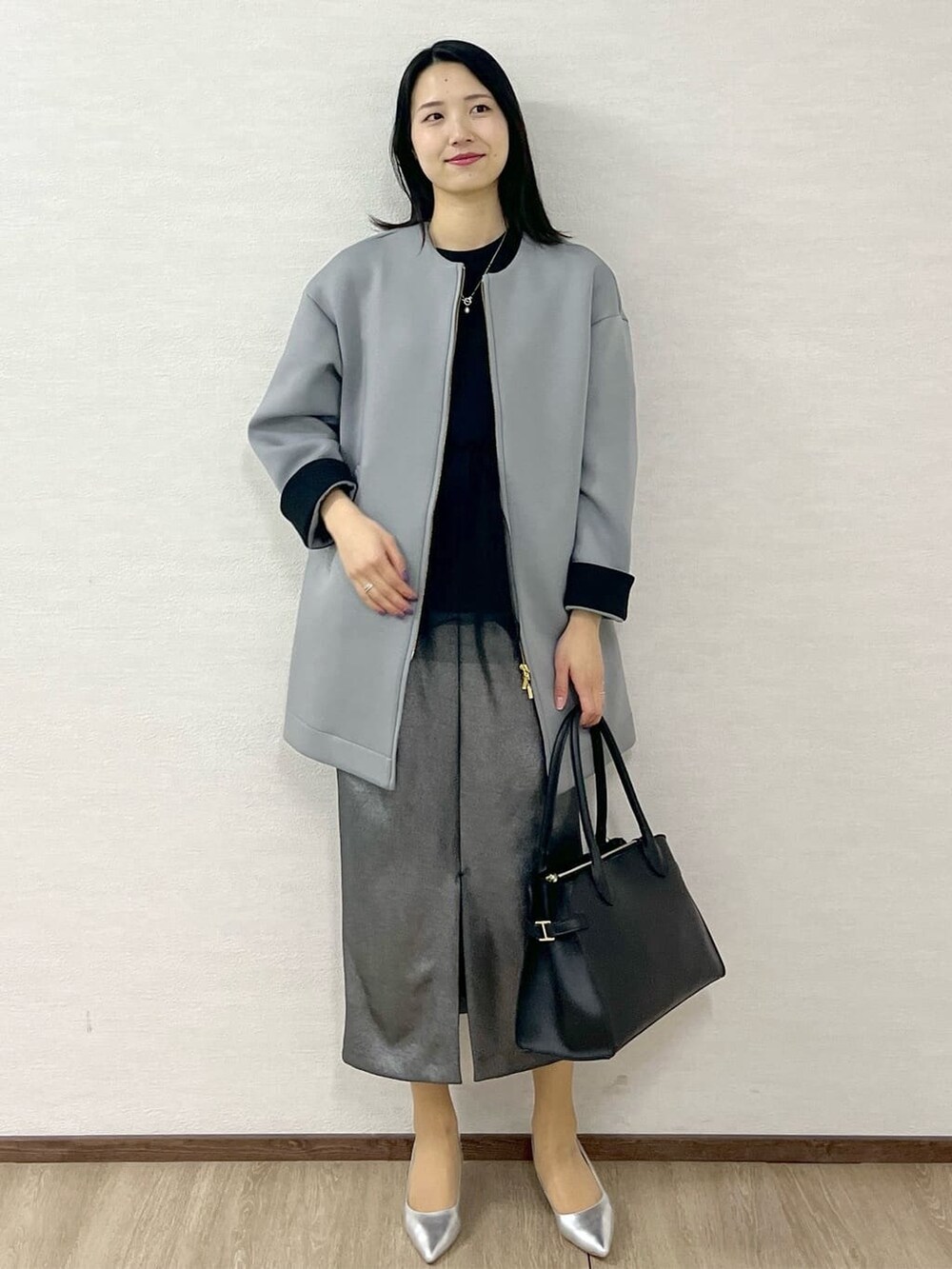 グレー系のノーカラーコート、ブラック系のTシャツ/カットソー、ブラック系のスカートを着用したレディースの冬コーディネートの2枚目の写真