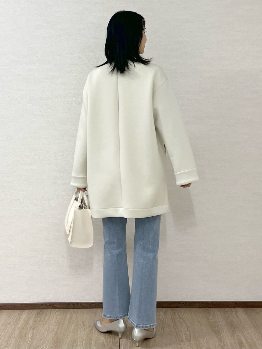 ホワイト系のノーカラーコート、シルバー系のニット/セーター、ブルー系のデニムパンツを着用したレディースの冬コーディネートの4枚目の写真