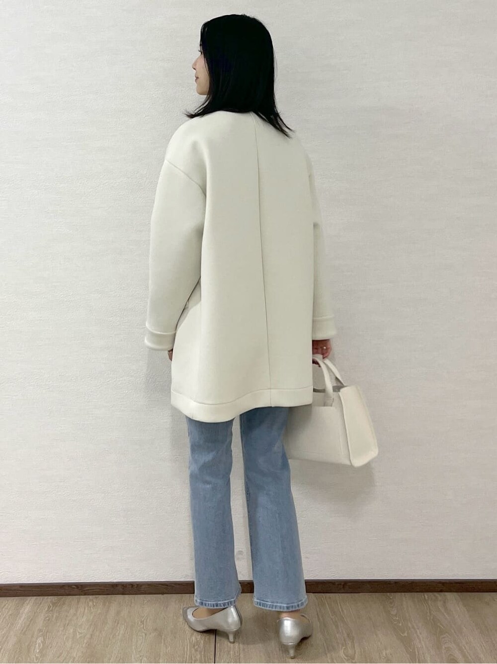 ホワイト系のノーカラーコート、ブルー系のニット/セーター、ブルー系のデニムパンツを着用したレディースの冬コーディネートの6枚目の写真