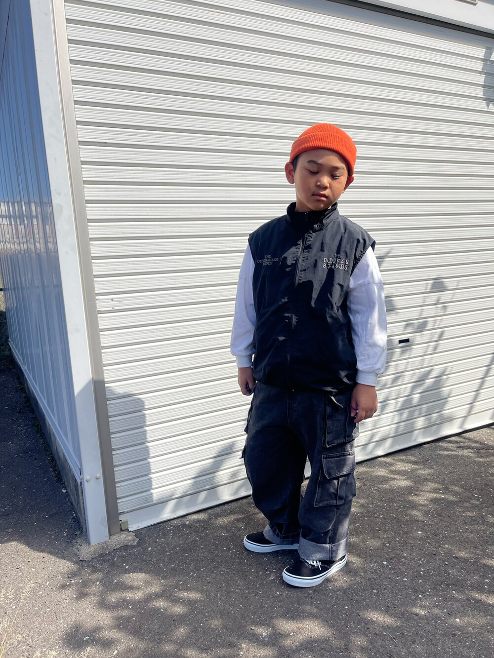 ブラック系のダウンベスト、ブラック系のデニムパンツ、オレンジ系のニットキャップ/ビーニーを着用したキッズの秋コーディネートの4枚目の写真