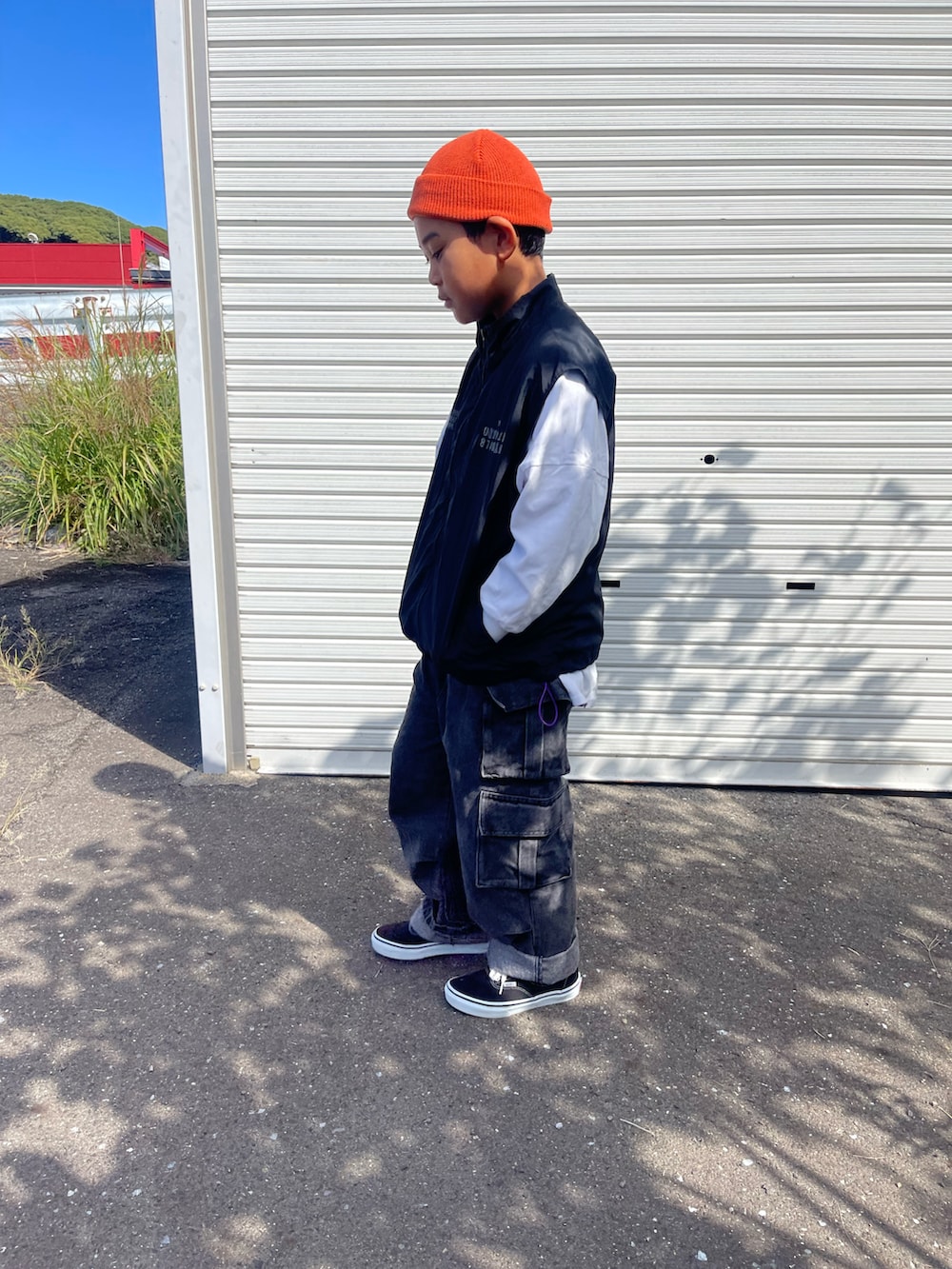ブラック系のダウンベスト、ブラック系のデニムパンツ、オレンジ系のニットキャップ/ビーニーを着用したキッズの秋コーディネートの3枚目の写真