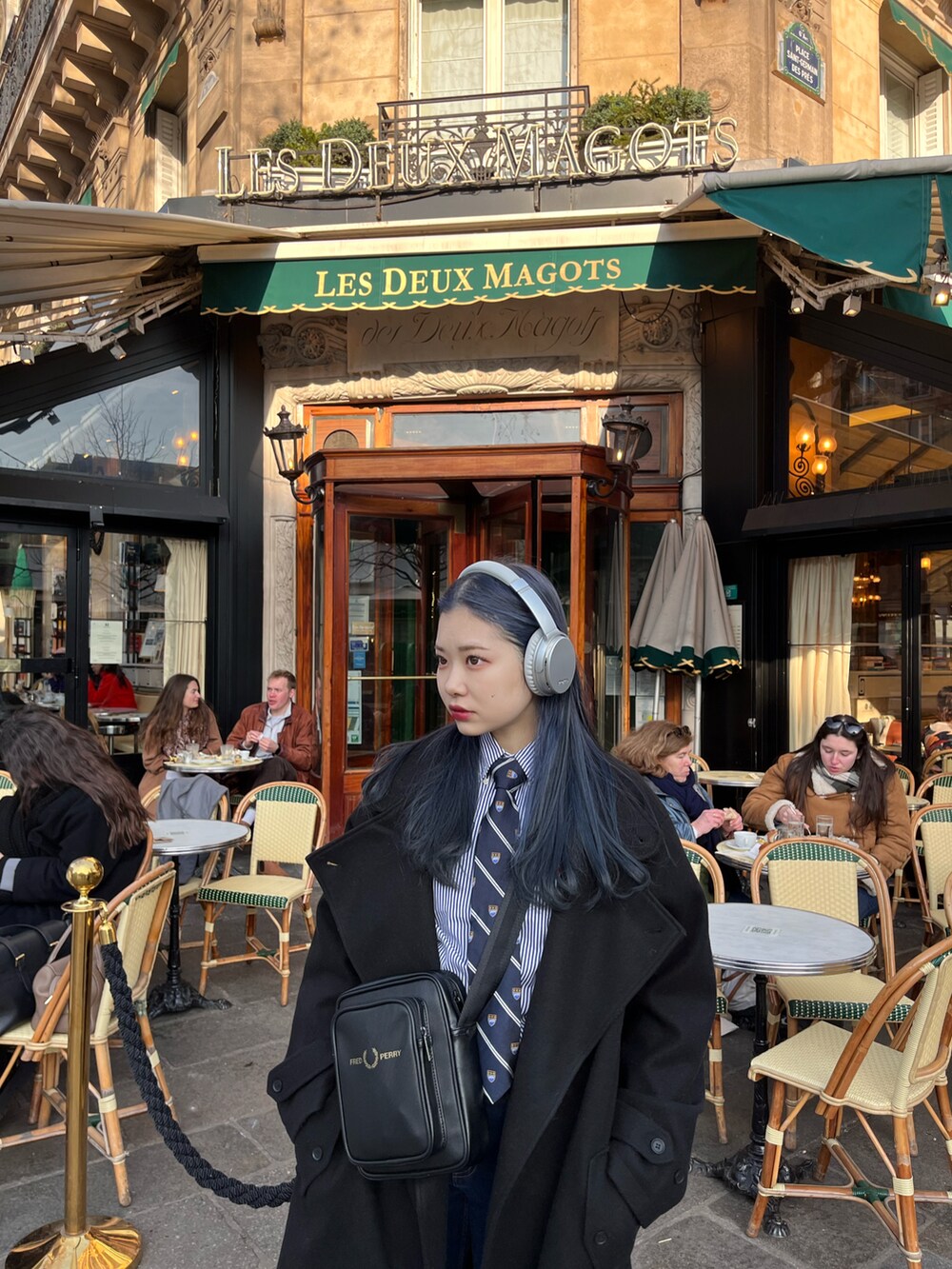 ブラック系のチェスターコート、ブラック系のショルダーバッグ、ブラック系のスニーカーを着用したレディースの冬コーディネートの3枚目の写真