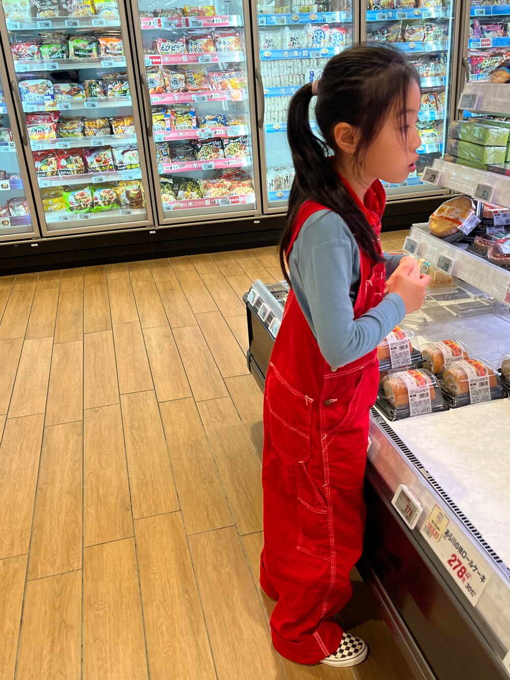 グリーン系のスタジャン、ベージュ系のスウェット、レッド系のオールインワン・サロペットを着用したキッズの春コーディネートの2枚目の写真