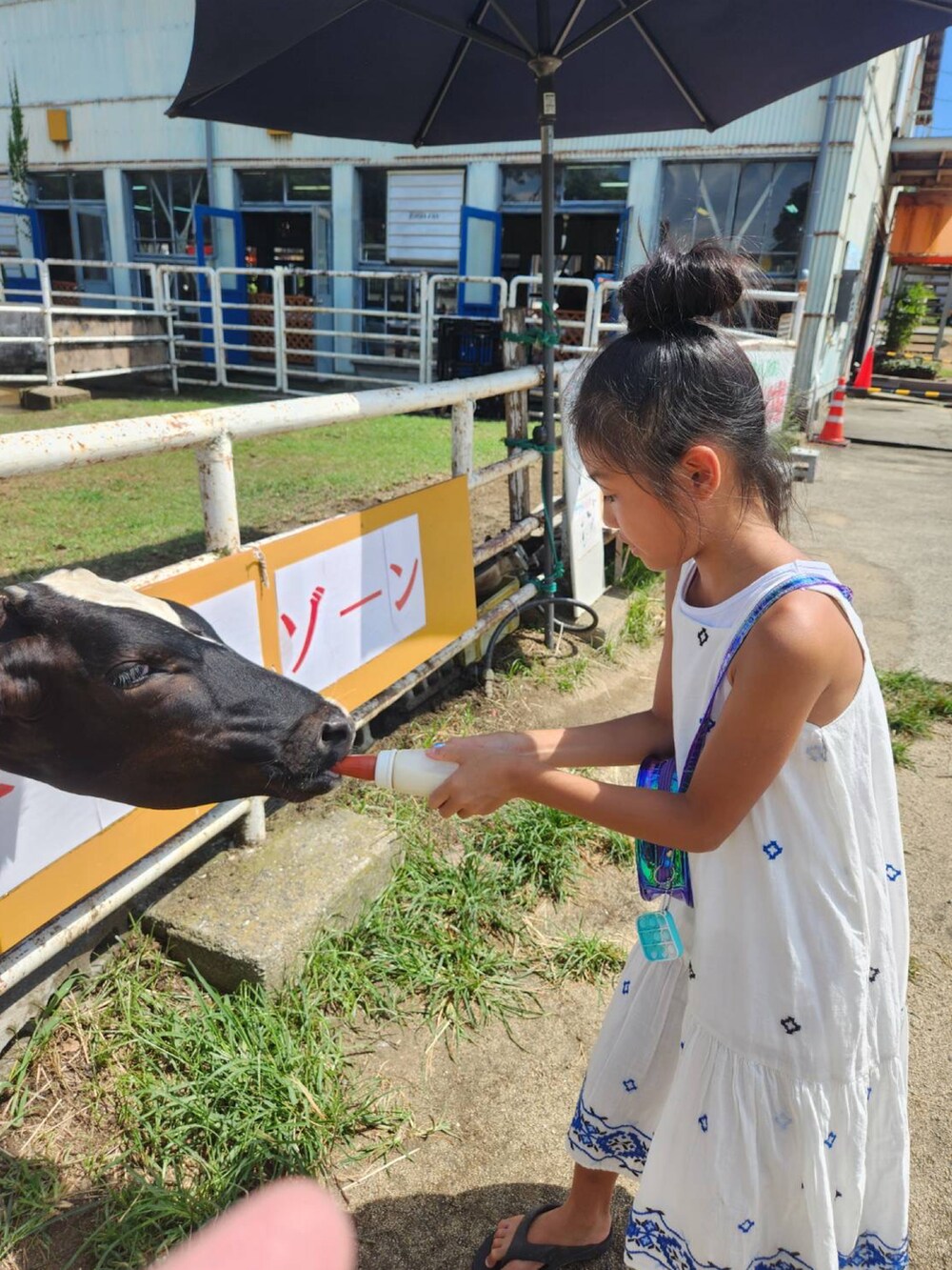 ホワイト系のワンピース、ブラック系のビーチサンダル、ブルー系のショルダーバッグを着用したキッズの夏コーディネートの4枚目の写真
