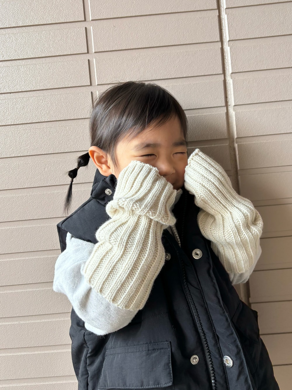 ブラック系のダウンベスト、ブラック系のブーツ、ベージュ系のアームカバーを着用したキッズの冬コーディネートの3枚目の写真