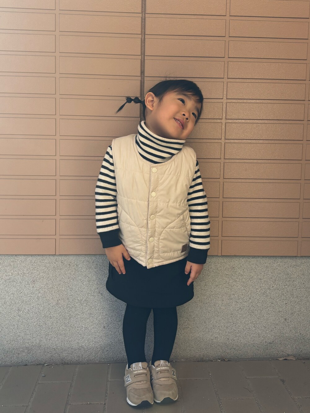 ベージュ系のダウンベスト、ブラック系のニット/セーター、ブラック系のスカートを着用したキッズの冬コーディネートの2枚目の写真
