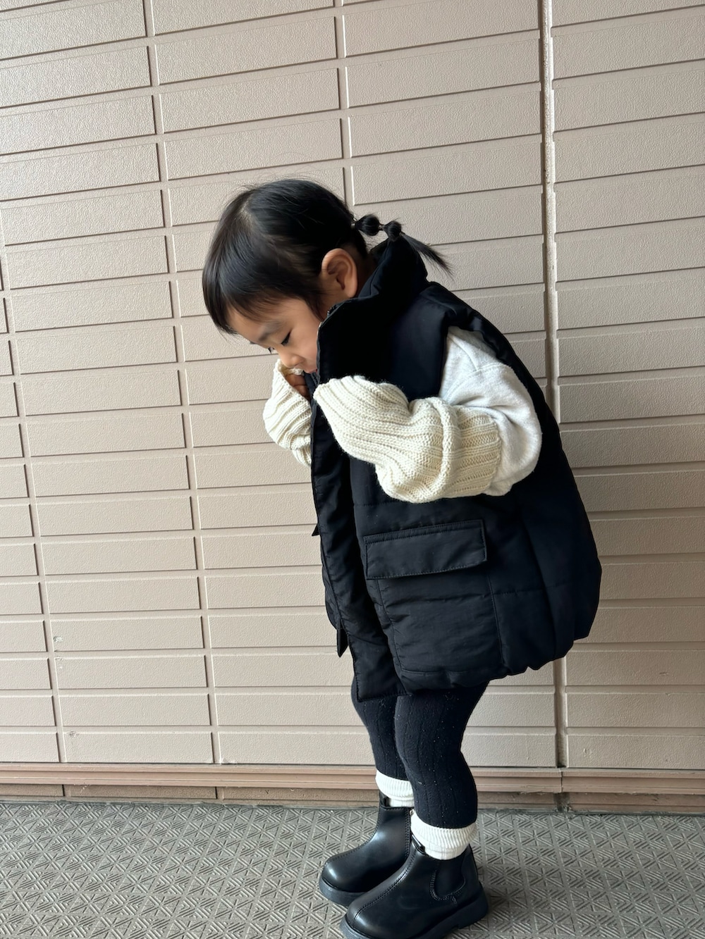 ブラック系のダウンベスト、ブラック系のブーツ、ベージュ系のアームカバーを着用したキッズの冬コーディネートの2枚目の写真
