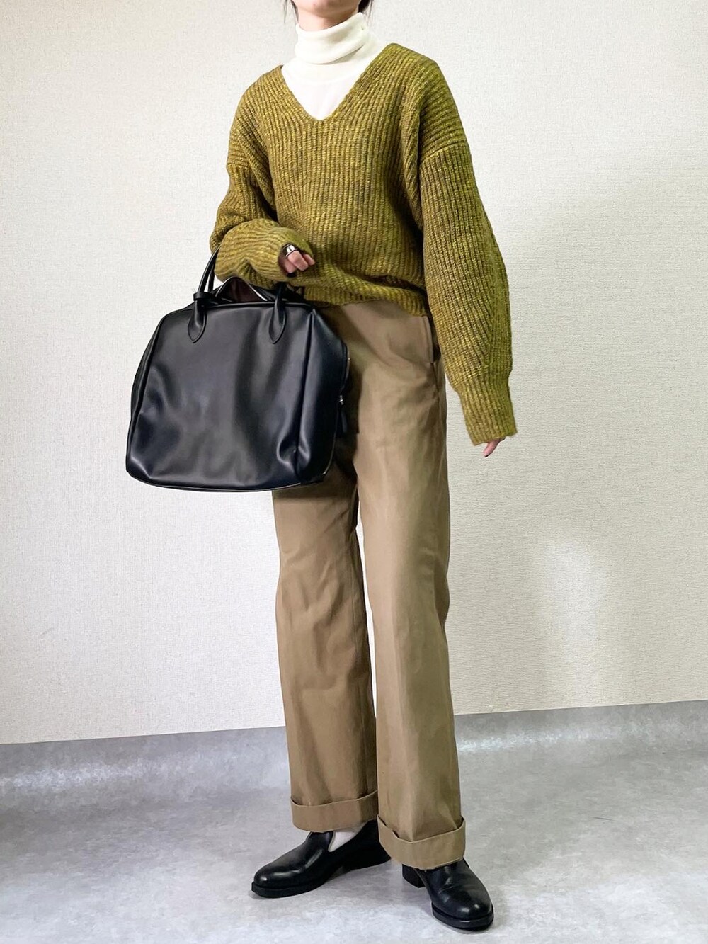 ブラウン系のステンカラーコート、イエロー系のニット/セーター、ベージュ系のチノパンツを着用したレディースの冬コーディネートの2枚目の写真