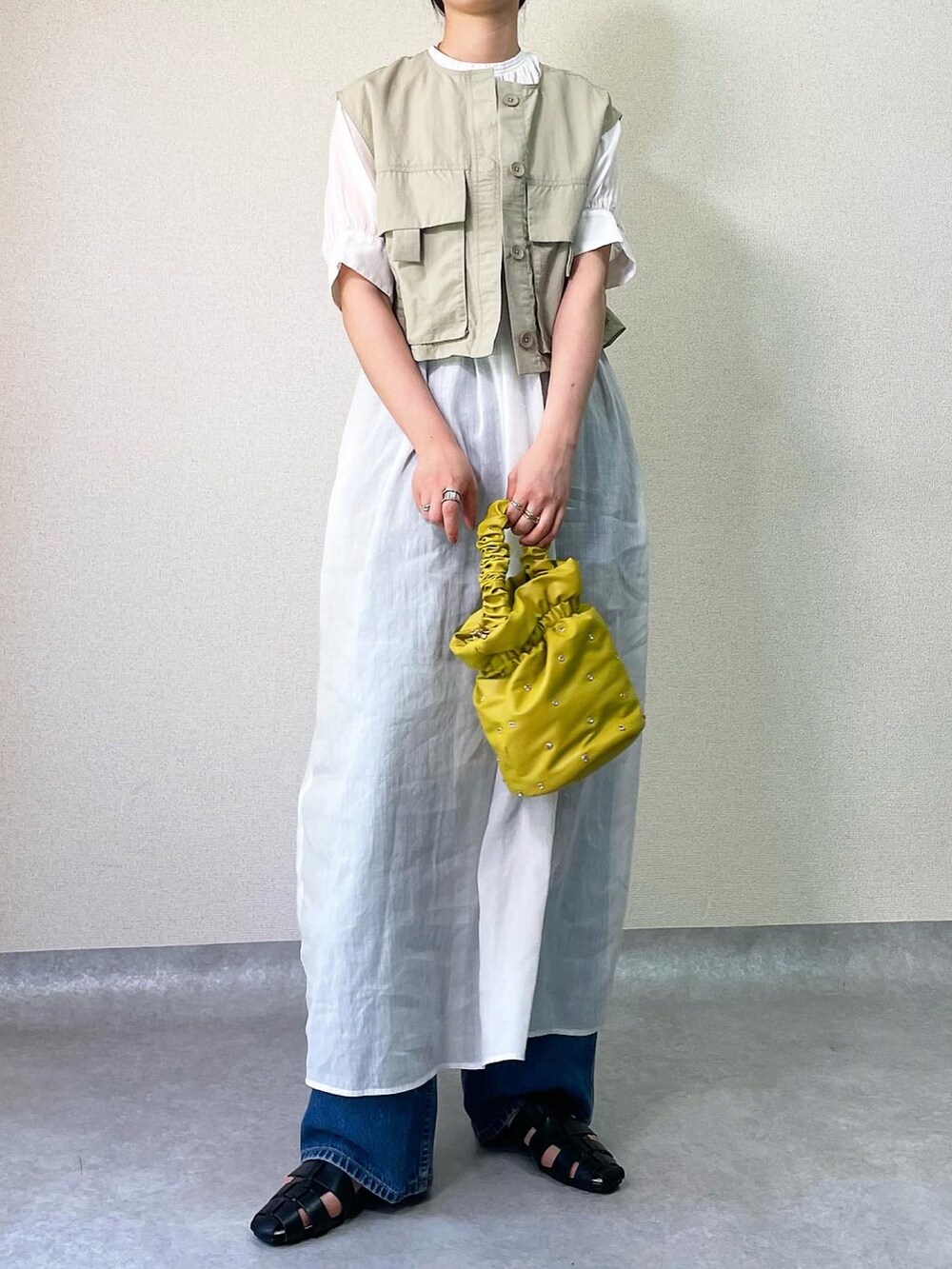 イエロー系のバッグ、ホワイト系のワンピース、グリーン系のベストを着用したレディースの春コーディネートの2枚目の写真