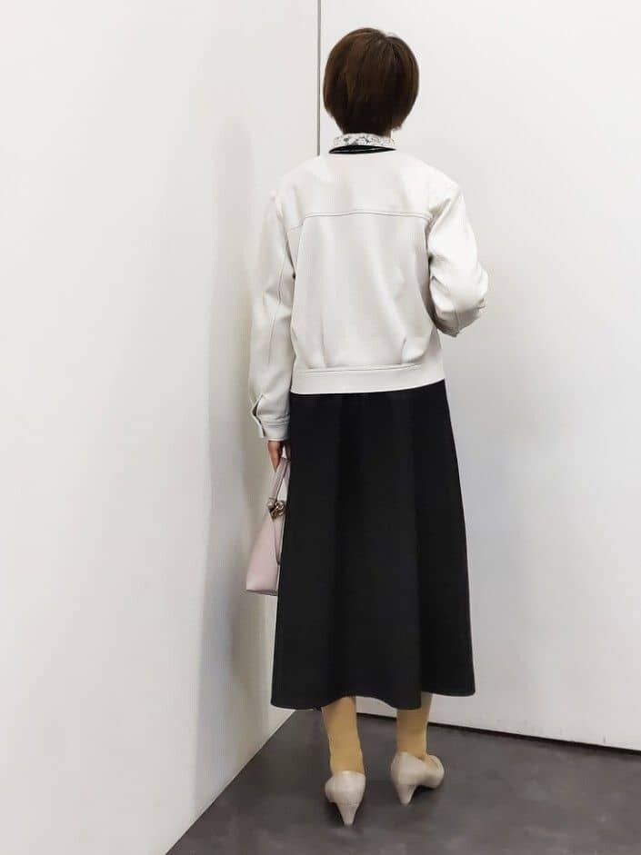 ホワイト系のノーカラージャケット、ブラック系のワンピース、ピンク系のハンドバッグを着用したレディースの冬コーディネートの3枚目の写真