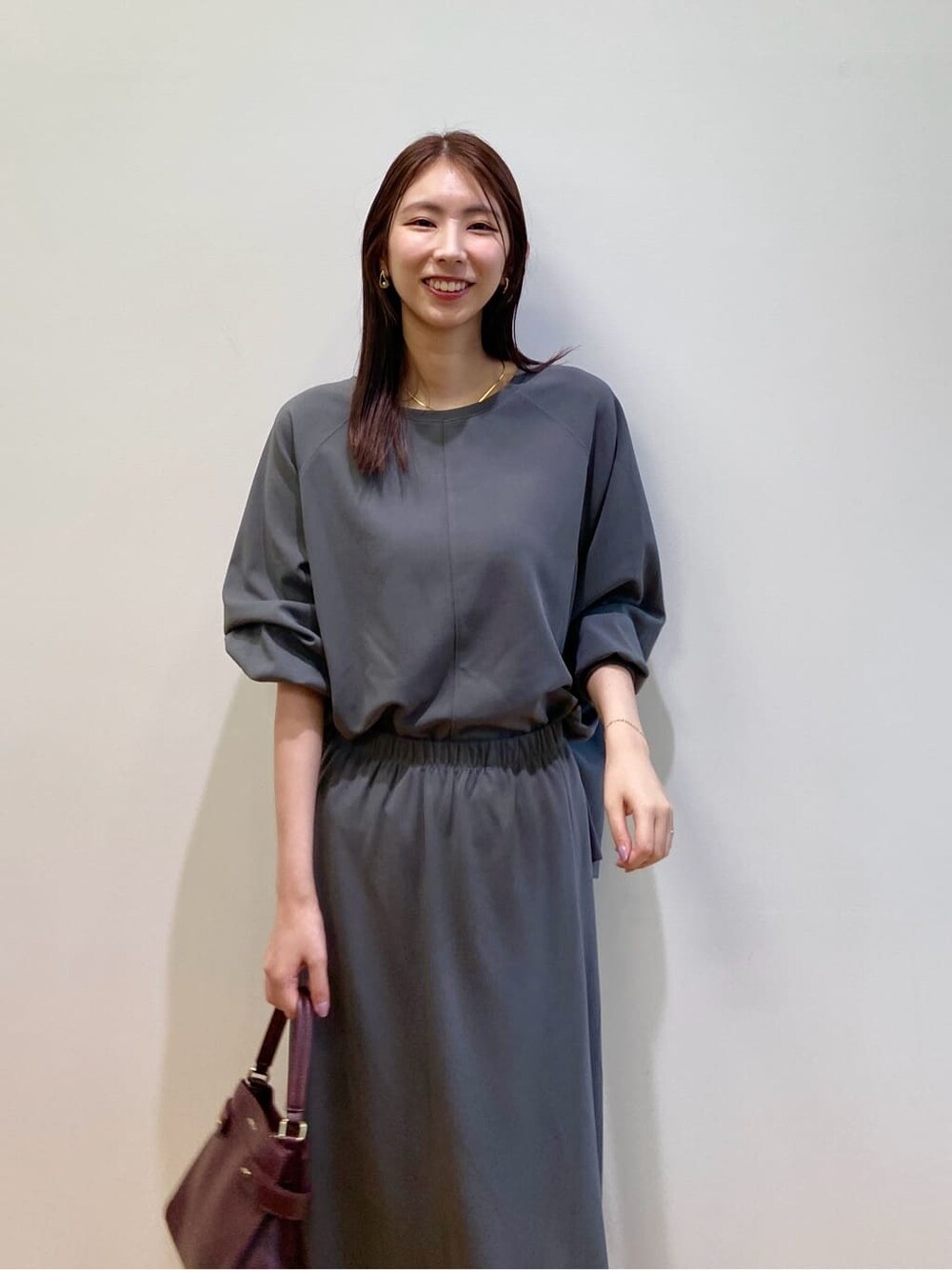 グレー系のセットアップ、レッド系のショルダーバッグ、レッド系のパンプスを着用したレディースの秋コーディネートの7枚目の写真