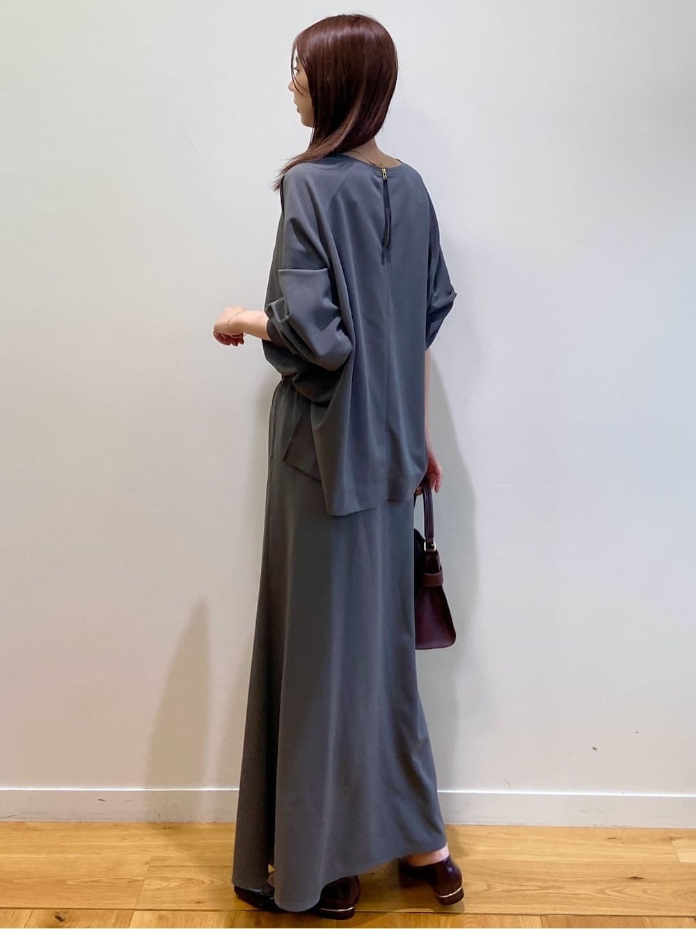 グレー系のセットアップ、レッド系のショルダーバッグ、レッド系のパンプスを着用したレディースの秋コーディネートの5枚目の写真