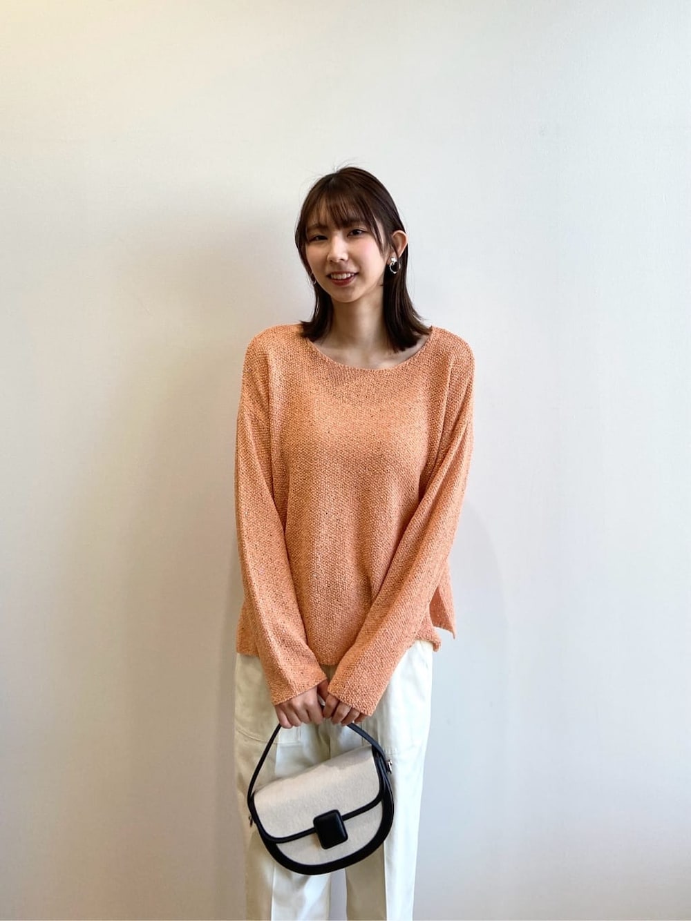 オレンジ系のニット/セーター、ホワイト系のその他パンツ、ブラック系のショルダーバッグを着用したレディースの春コーディネートの4枚目の写真
