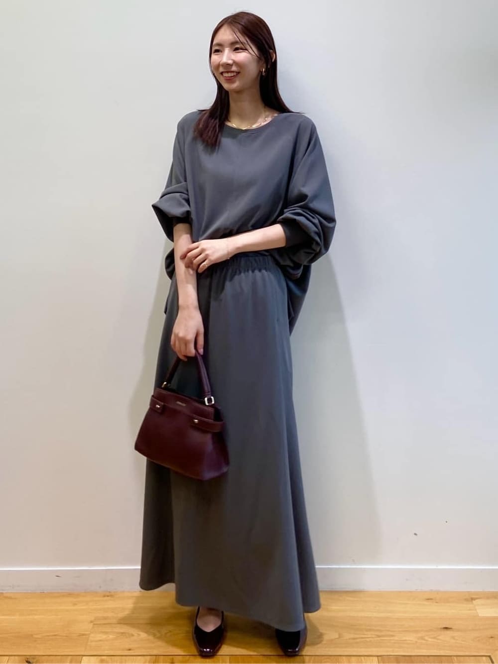 グレー系のセットアップ、レッド系のショルダーバッグ、レッド系のパンプスを着用したレディースの秋コーディネートの3枚目の写真
