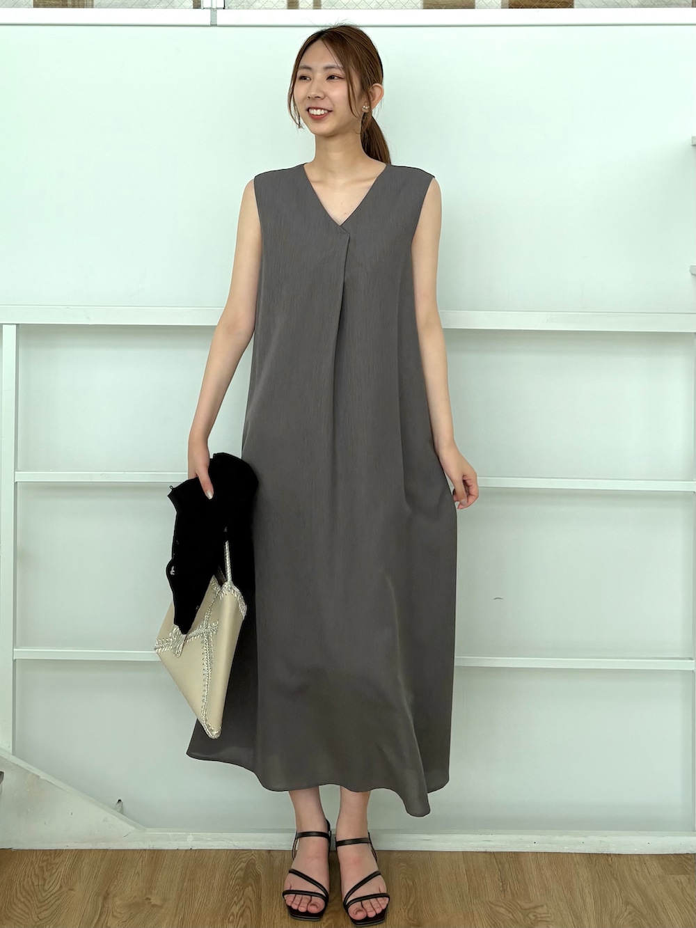 グレー系のワンピース、ホワイト系のハンドバッグ、ブラウン系のサンダルを着用したレディースの夏コーディネートの2枚目の写真