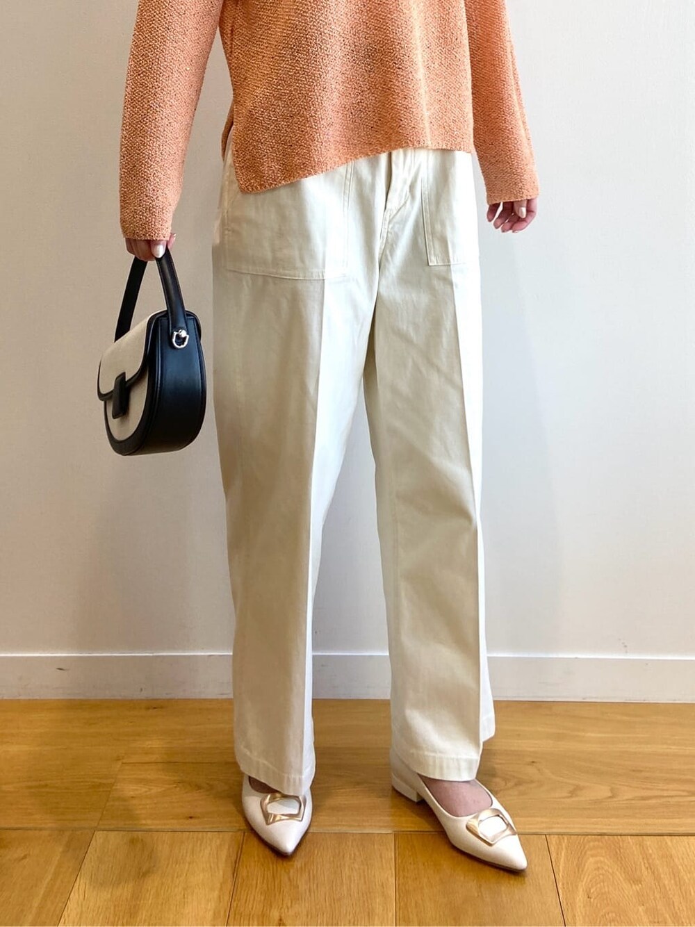 オレンジ系のニット/セーター、ホワイト系のその他パンツ、ブラック系のショルダーバッグを着用したレディースの春コーディネートの7枚目の写真