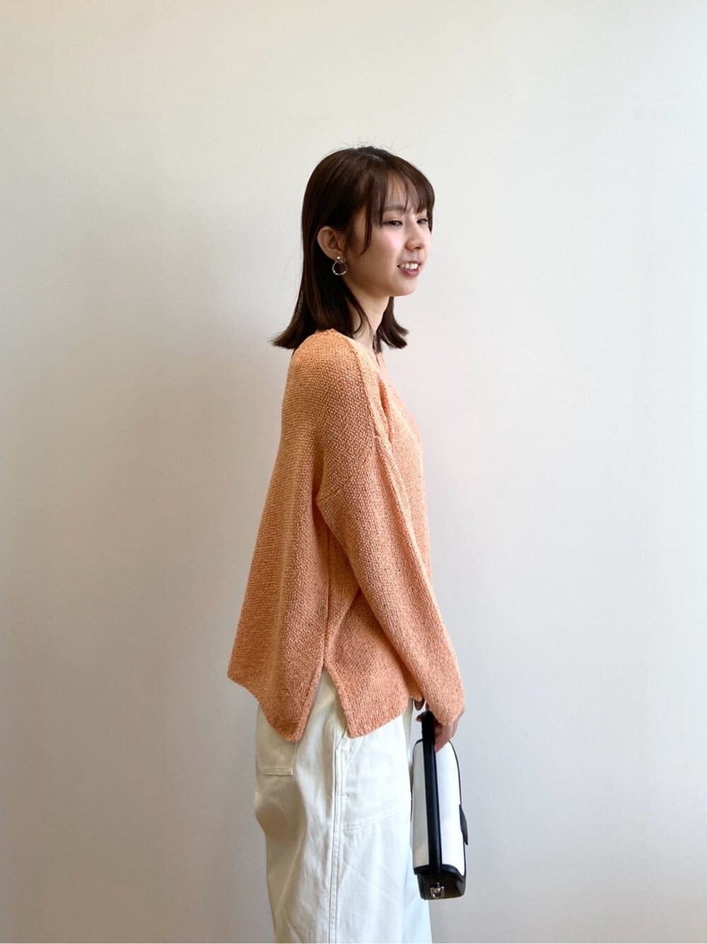 オレンジ系のニット/セーター、ホワイト系のその他パンツ、ブラック系のショルダーバッグを着用したレディースの春コーディネートの5枚目の写真