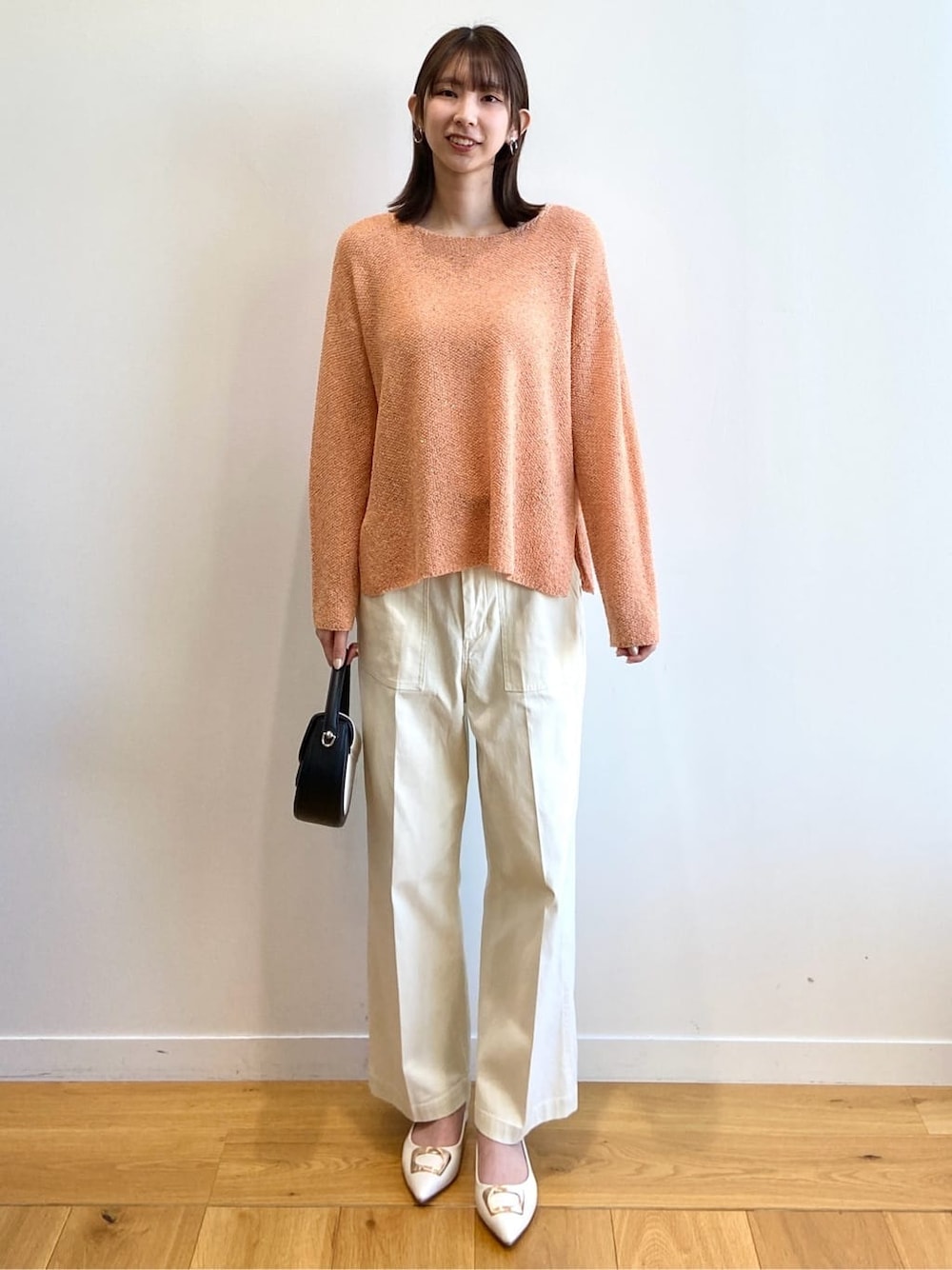 オレンジ系のニット/セーター、ホワイト系のその他パンツ、ブラック系のショルダーバッグを着用したレディースの春コーディネートの2枚目の写真