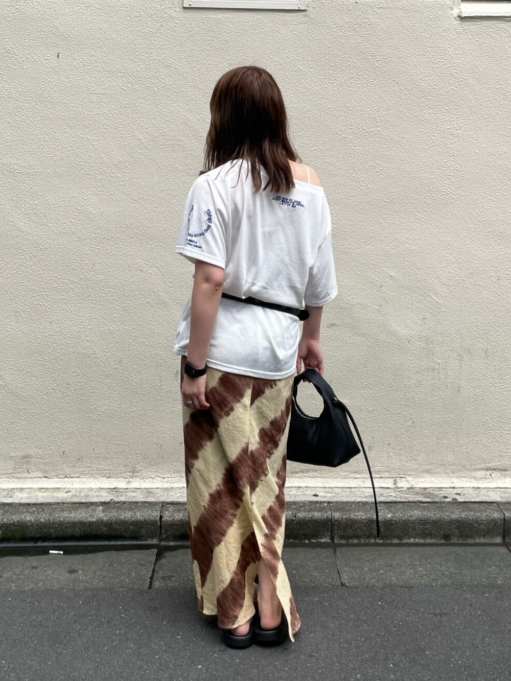 ブラウン系のスカート、ブラック系のハンドバッグ、ホワイト系のTシャツ/カットソーを着用したレディースの夏コーディネートの3枚目の写真
