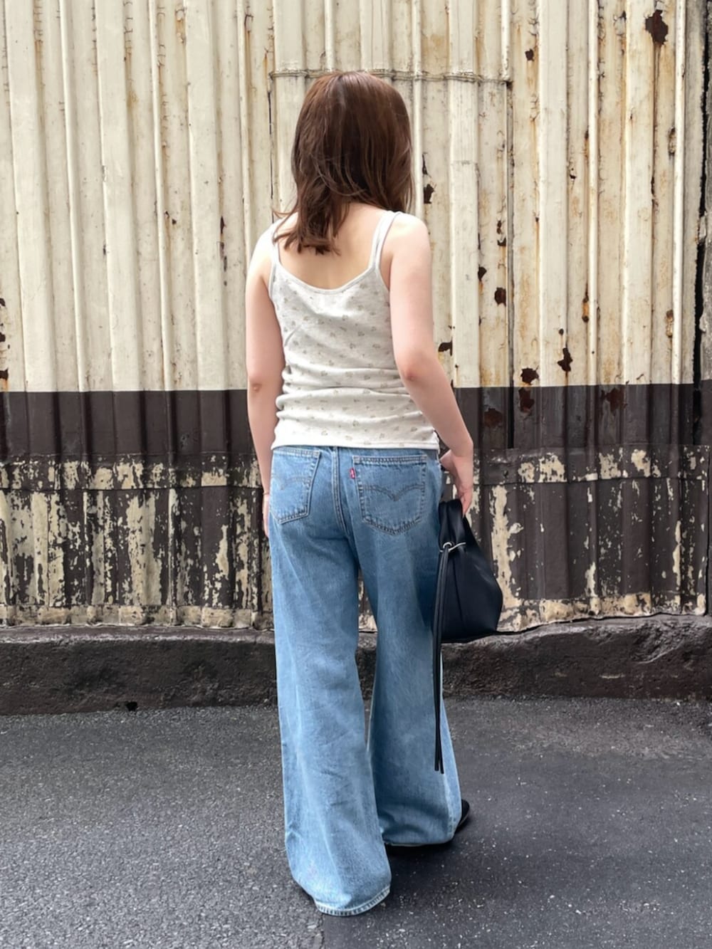 ブラック系のハンドバッグ、ブルー系のデニムパンツ、グレー系のキャミソールを着用したレディースの夏コーディネートの3枚目の写真