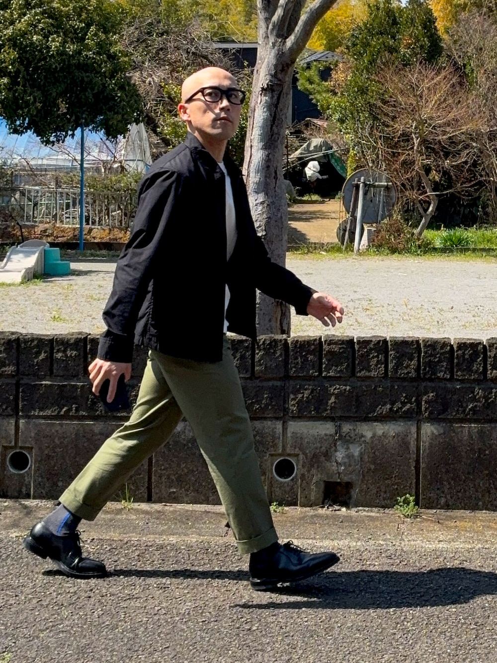 ブラック系のドレスシューズ、グリーン系のスラックス、ブラック系のブルゾンを着用したメンズの春コーディネートの2枚目の写真