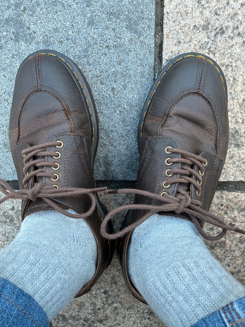 グレー系のニット/セーター、ブラック系のチェスターコート、ブルー系のデニムパンツを着用したメンズの春コーディネートの3枚目の写真