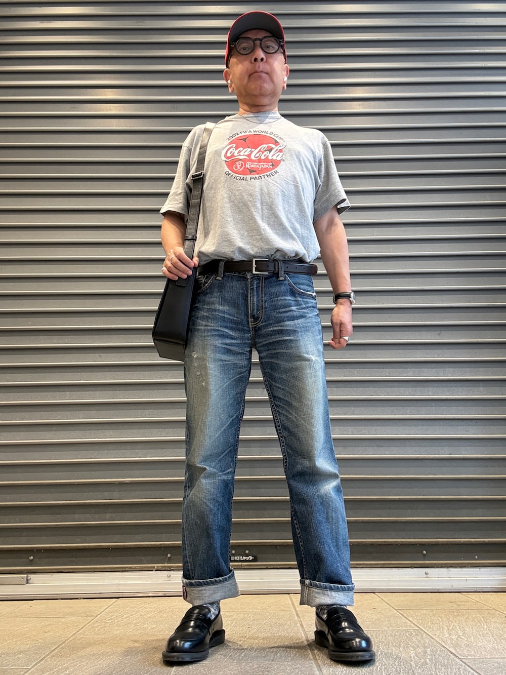 ブルー系のデニムパンツ、グレー系のTシャツ/カットソー、ブラック系のショルダーバッグを着用したメンズの夏コーディネートの2枚目の写真