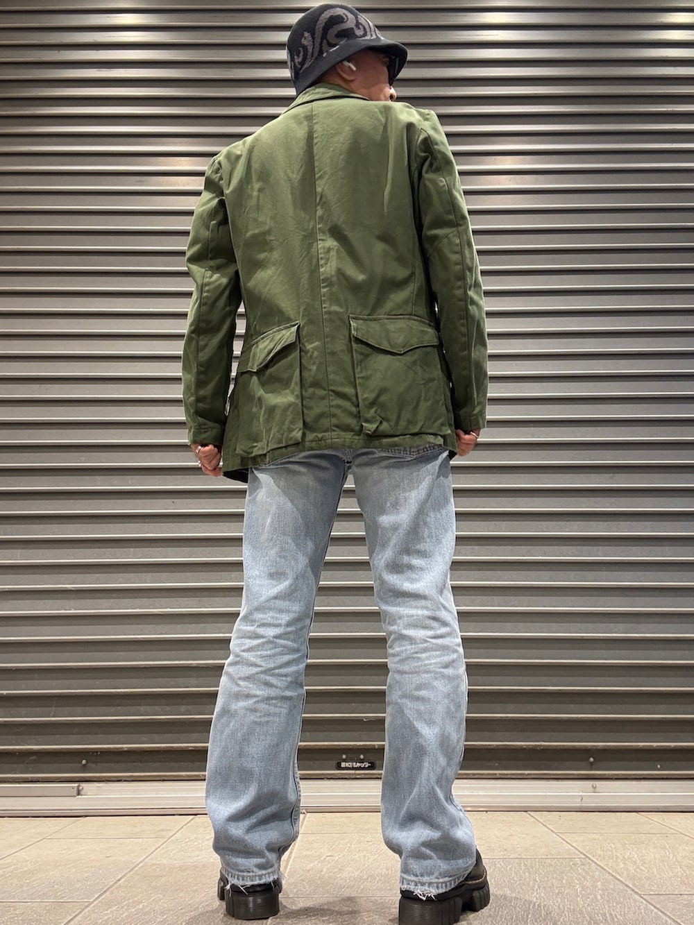 ブラック系のローファー、ベージュ系のTシャツ/カットソー、グリーン系のミリタリージャケットを着用したメンズの春コーディネートの3枚目の写真