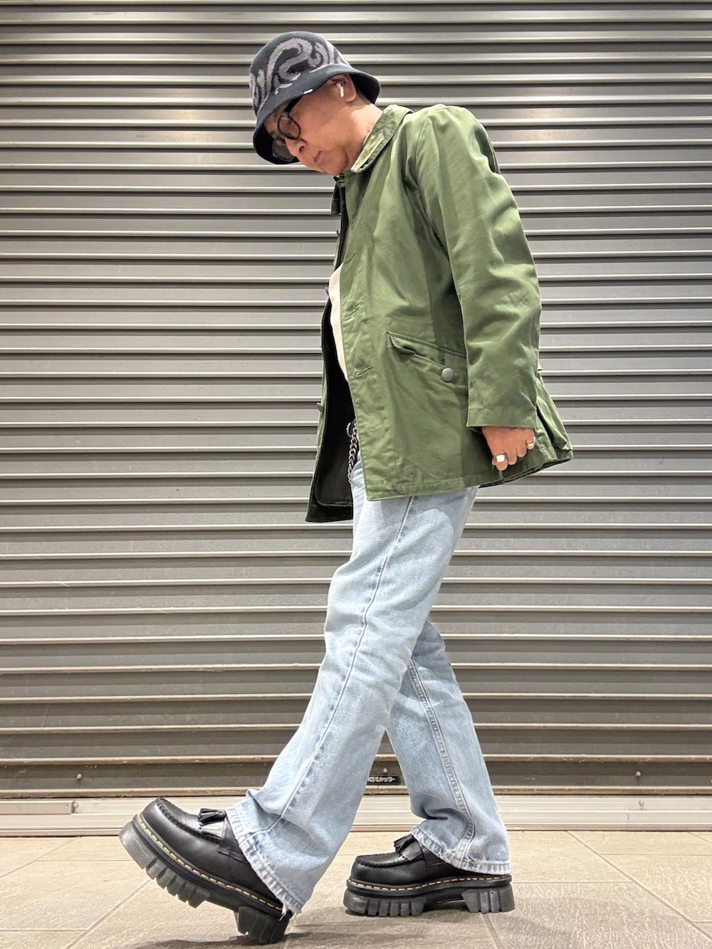 ブラック系のローファー、ベージュ系のTシャツ/カットソー、グリーン系のミリタリージャケットを着用したメンズの春コーディネートの2枚目の写真