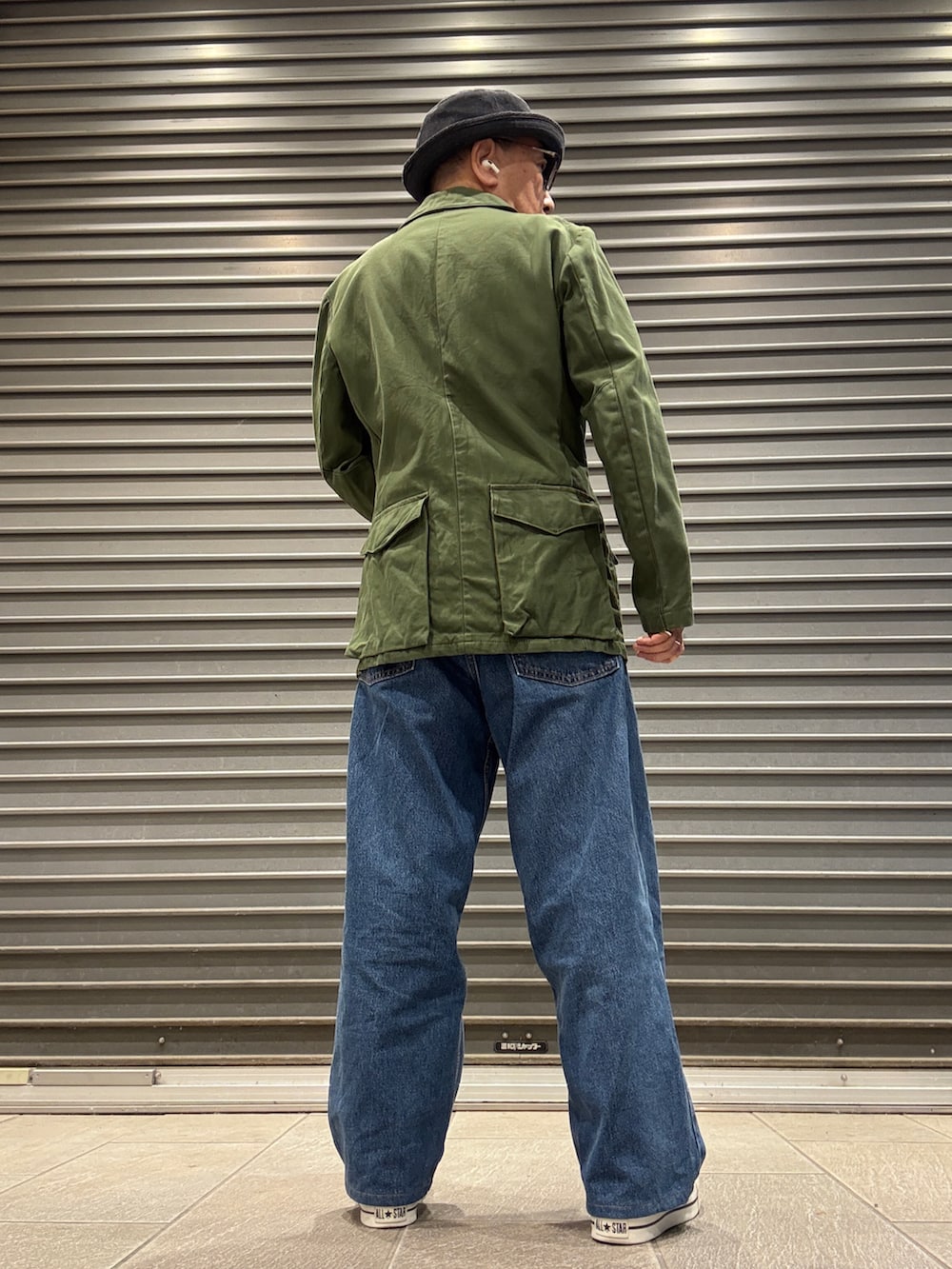 グリーン系のミリタリージャケット、レッド系のスウェット、ブルー系のデニムパンツを着用したメンズの秋コーディネートの2枚目の写真