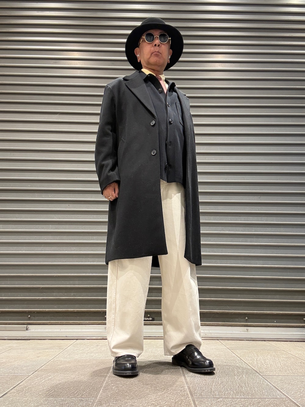 ブラック系のチェスターコート、ブラック系のカーディガン/ボレロ、イエロー系のシャツ/ブラウスを着用したメンズの秋コーディネートの2枚目の写真