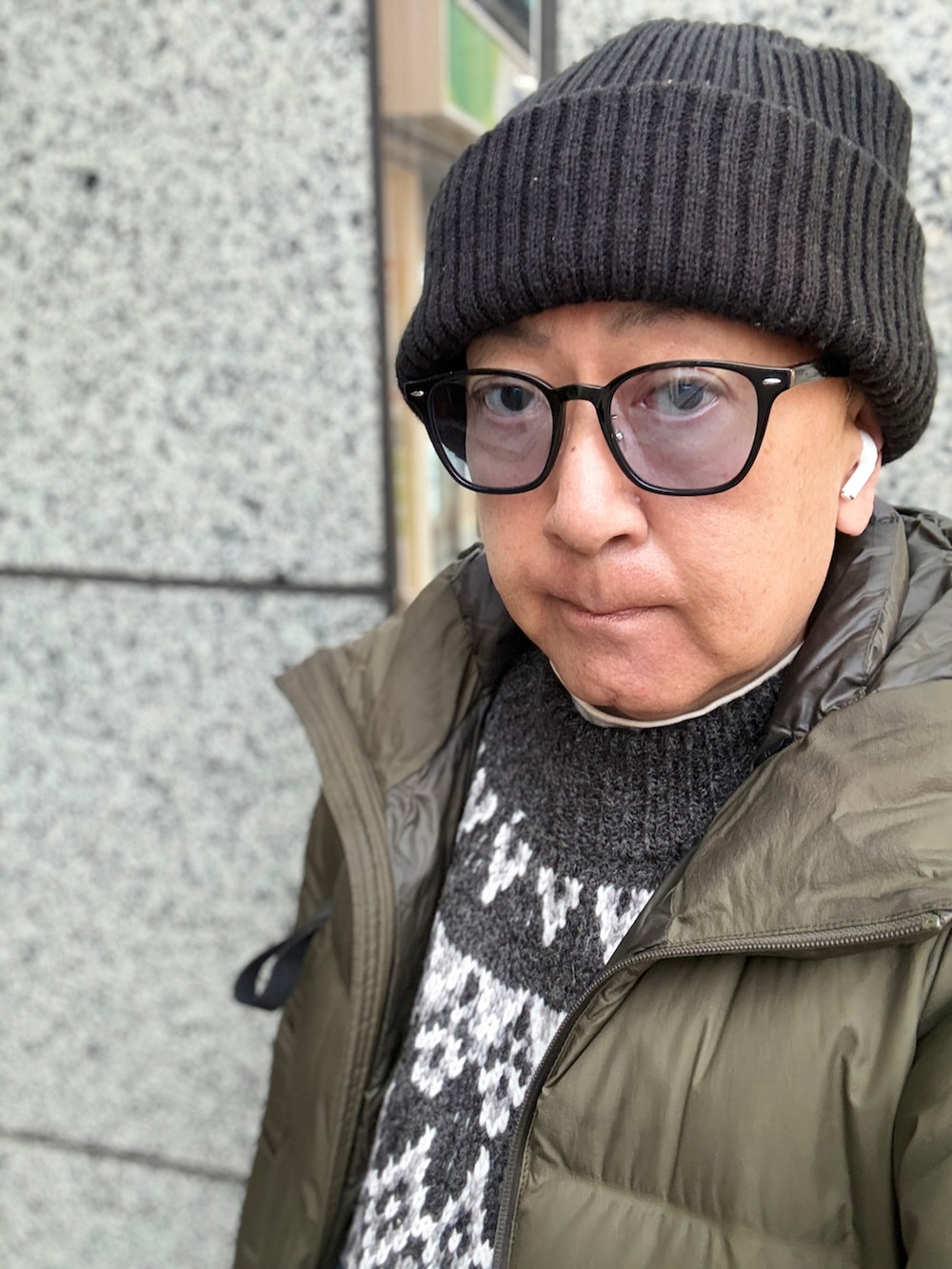 グレー系のニット/セーター、グリーン系のダウンジャケット/コート、ブラック系のバックパック/リュックを着用したメンズの冬コーディネートの2枚目の写真