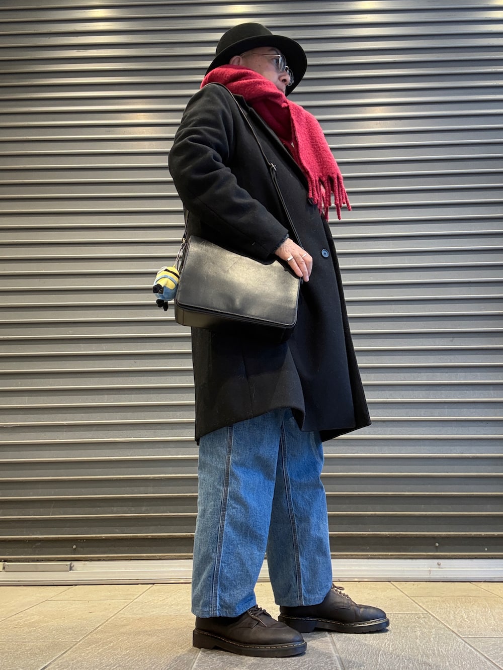 グレー系のニット/セーター、ブラック系のチェスターコート、ブルー系のデニムパンツを着用したメンズの春コーディネートの2枚目の写真