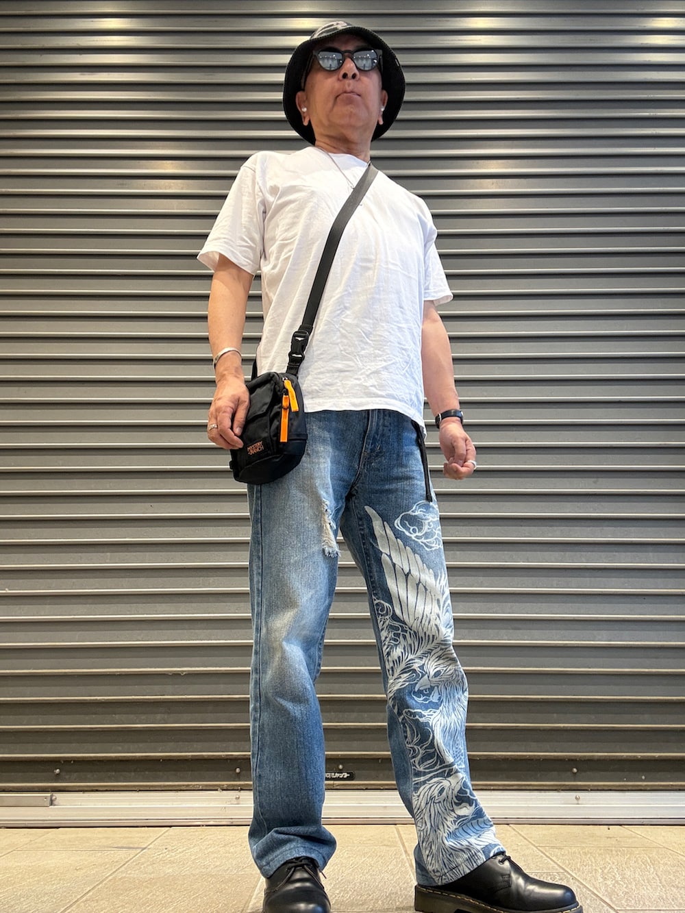 ブルー系のデニムパンツ、ホワイト系のTシャツ/カットソー、ブラック系のショルダーバッグを着用したメンズの夏コーディネートの2枚目の写真