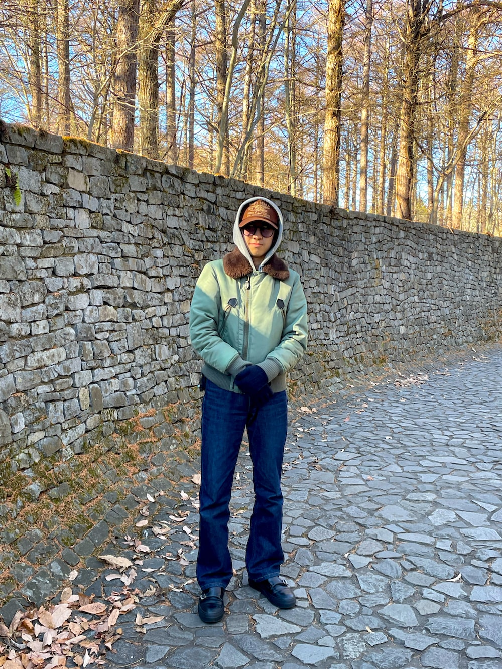 グリーン系のミリタリージャケット、ブルー系のデニムパンツ、ブラック系のスニーカーを着用したメンズの冬コーディネートの3枚目の写真