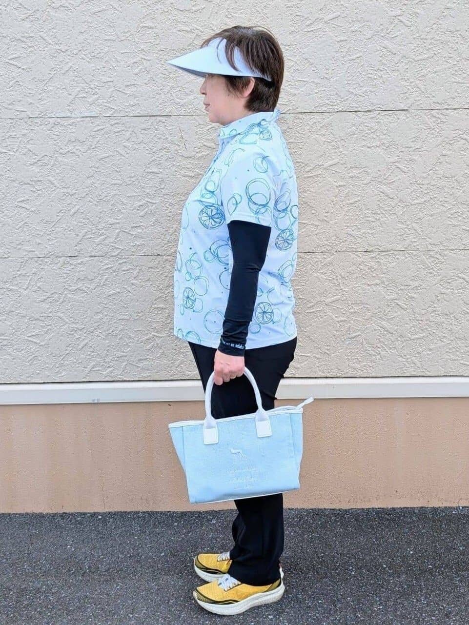 ブルー系のポロシャツ、ブラック系のその他パンツ、ホワイト系のサンバイザーを着用したレディースの春コーディネートの2枚目の写真