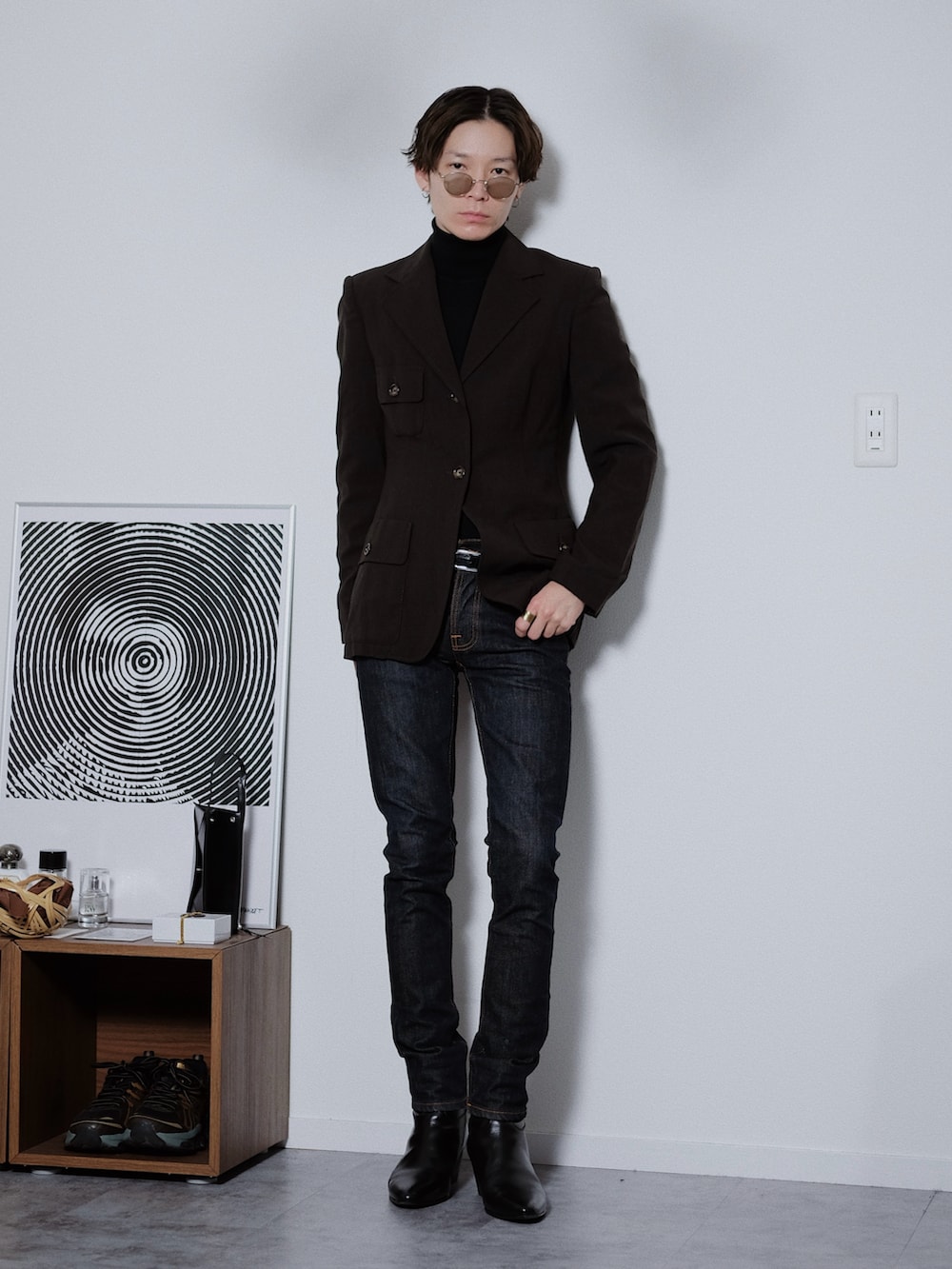 ブラウン系のテーラードジャケット、ブラック系のニット/セーター、ブルー系のデニムパンツを着用したメンズの春コーディネートの2枚目の写真